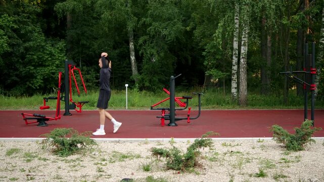 Athlete awlking and stretching before a work out on an outdoor training ground. Man warming up for a training session on an outdoor gym. Athletic man doing dynamic warm up walks outdoors.