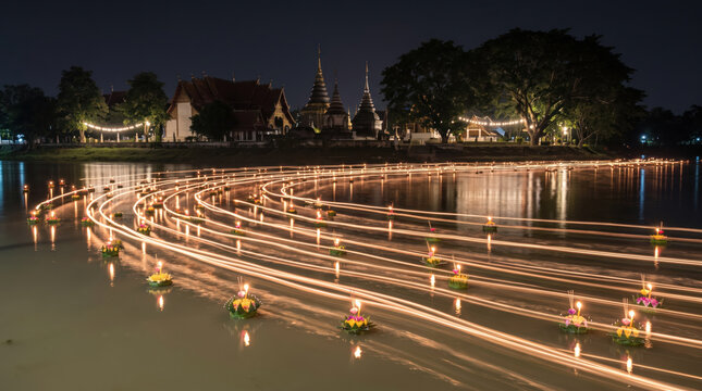 Long exposure night photograph of traditional floating candle boat along peaceful river, glowing reflection creating scale and serenity.
