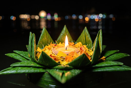 Macro candle photography featuring glowing flame in handcrafted banana leaf flower, surrounded by yellow petals and water reflections.