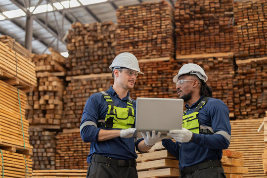 Workers discuss tasks in a warehouse with pallets stacked high in the background