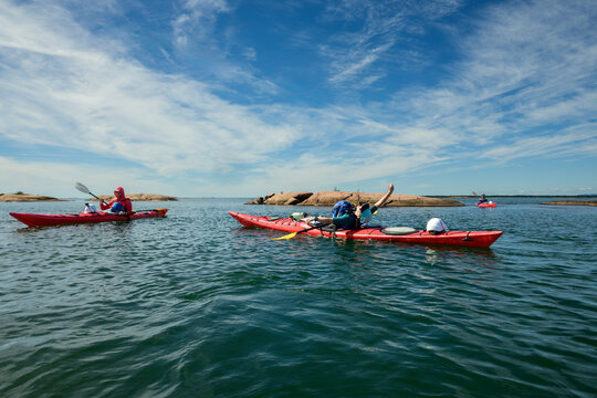 Sea kayaker leaning back and stretching an arm skyward on red kayak with paddling partners nearby, blue sky copy space, Georgian Bay, Ontario