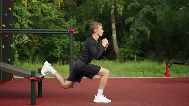 Young man learning to do a Bulgarian split squat with his back foot elevated on a bench at an outdoor sports ground. Athlete trying to do a split squat and loosing balance.