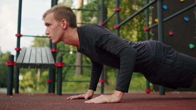 Man doing push-ups at an outdoor fitness ground. Young athletic man doing push-ups at an outside gym. Athlete doing classic floor push-ups during a street workout session. Sport activity.