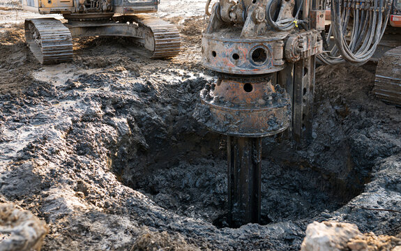 Heavy drilling machine excavating deep circular hole in muddy ground with construction equipment operating for foundation and infrastructure work
