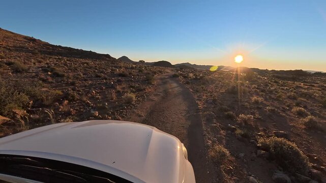 A white car is driving along a narrow, bumpy road with a poor surface in the African savanna.