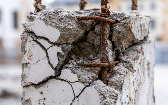 Severely damaged concrete pillar shows large cracks, spall. Rusted steel rebar mesh exposed inside broken cement column. Industrial infrastructure decay at construction site abandoned building.