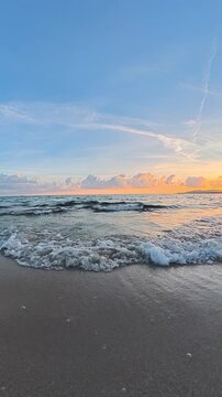 Vertical POV walk parallel to the shoreline at sunset, capturing waves breaking on the beach with natural ocean sounds and warm golden evening light in Sardinia.