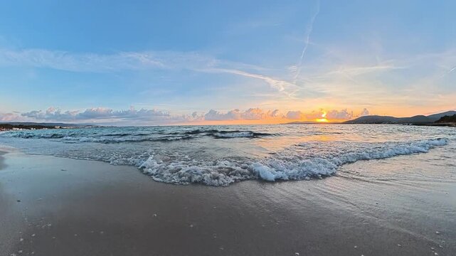 Horizontal POV walk parallel to the shoreline at sunset, capturing waves breaking on the beach with warm golden light and a peaceful Mediterranean coastal atmosphere in Sardinia.