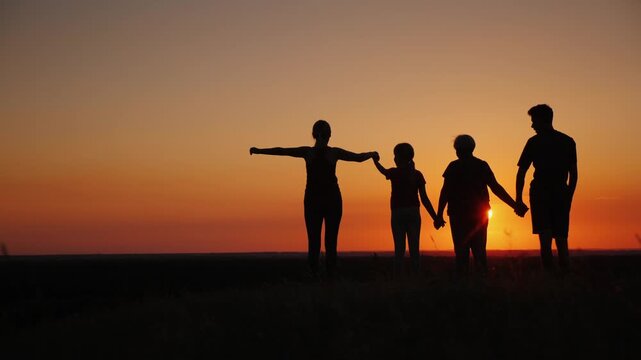 Silhouette of happy family with children holding hands at sunset, raising arms in success and unity, cinematic motion footage.