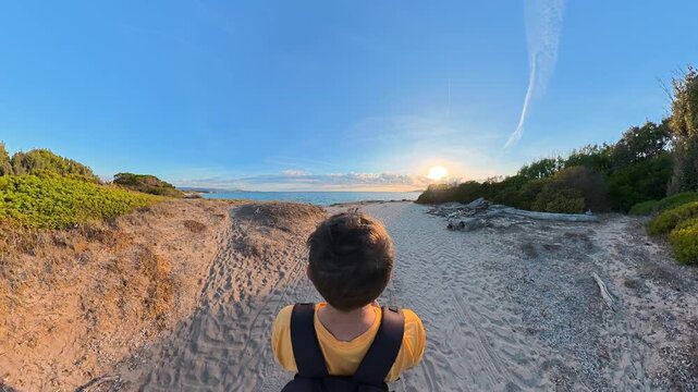 Third person view of a person walking along a sandy beach path toward the sea at sunset in Alghero, Sardinia, with natural sounds of wind and waves.