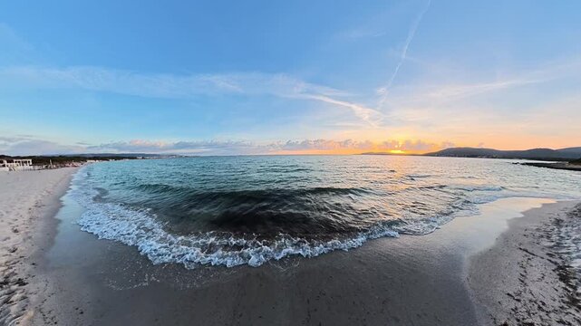 Low angle view filmed close to the shoreline as waves break on the beach, followed by a smooth upward camera movement revealing the sea and coastal landscape.