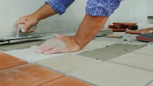 Craftsman carefully applies tile adhesive using trowel for floor tiling project.