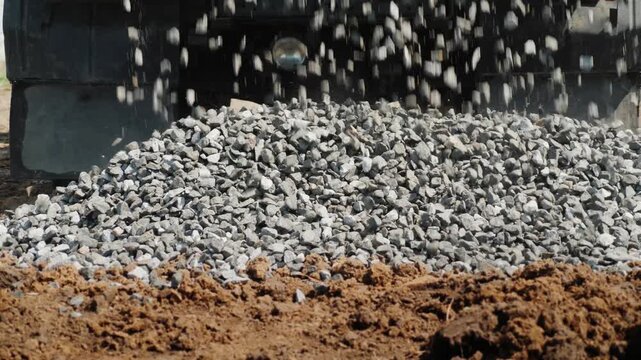 Close up shot of fresh gray gravel slowly falling on brown soil, captured with slow motion and cinematic footage, creating a dynamic construction scene.