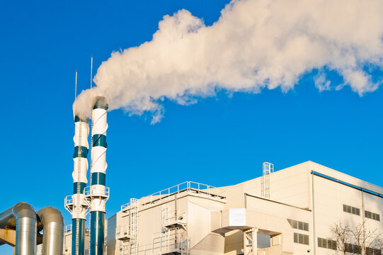 A heating plant and pipes emitting white smoke, with a pipeline in the foreground and a blue sky in the background