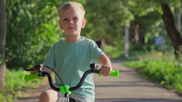 Close up of a kid riding a bicycle. Cute little blonde boy riding a bicycle in a sunny park. Young caucasian child learning to ride a bike outdoors.  Slow motion video of. a summer lifestyle concept
