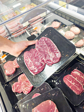 Shopper Choosing Fresh Raw Beef Steaks at Supermarket