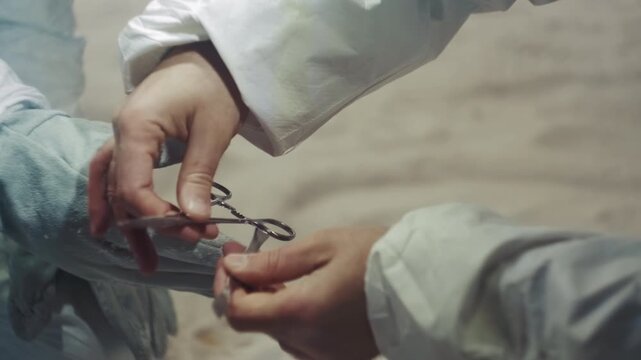 Researcher in protective suit removing glove to access frozen seedling inside abandoned house precise gloved hands unfasten seal with scissors and forceps sterile technique under pale winter light
