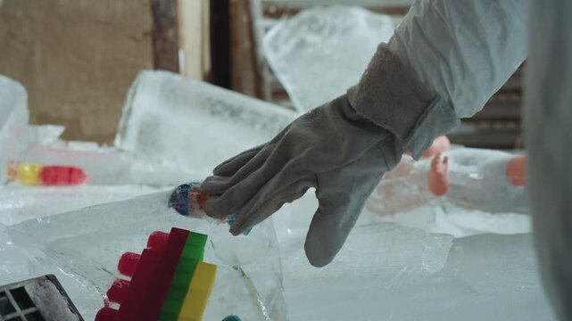 Gloved hand reaches for frozen toy in ruined house interior blocks and doll parts embedded in ice, scavenger in heavy mittens gently salvages childhood keepsake, frost coated surfaces, late light
