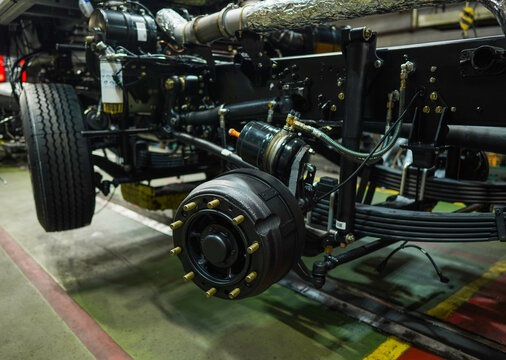 Heavy truck undercarriage with exposed suspension, brake drum, and exhaust system in industrial workshop setting