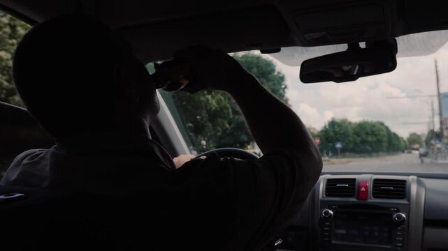 A male driver caught on camera drinking alcohol from a bottle while driving on a sunny day dangerous and irresponsible behavior.