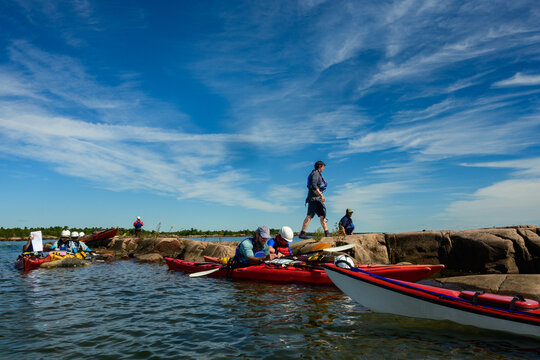 Sea kayak group taking a quick break on a small rocky island, paddler walking granite ridge under wispy clouds, copy space, Georgian Bay, Ontario