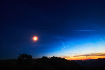 Moon on a twilight sky with stars, planets and landscape mountain silhouettes. © astrosystem