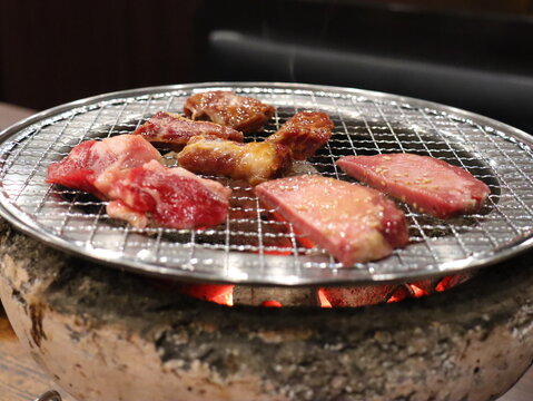 Sliced beef cooking on a round grill over glowing charcoal at a Japanese yakiniku restaurant