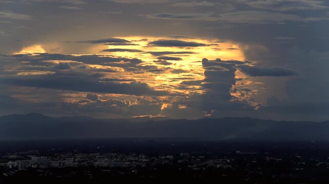 Time Lapse of Dramatic golden sunset glowing through dark clouds above a mountain landscape
