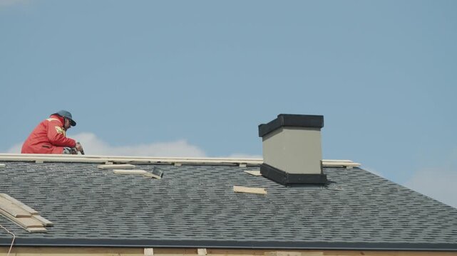 Professional roofer installing flexible bitumen shingles on new residential house roof on sunny day.