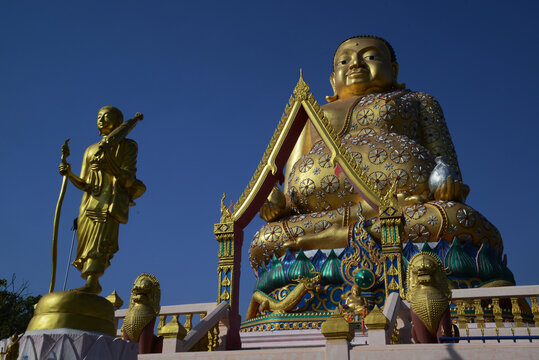 A large brilliantly gold-colored statue of Phra Maha Kaccayana Thera holding a holy water vessel representing the 76 provinces standing 20 meters tall at Wat Lang San Prasit.