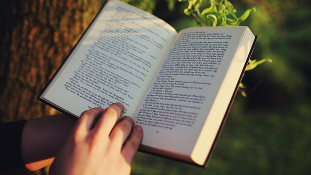 Person reading an open book outdoors in peaceful natural sunlight.