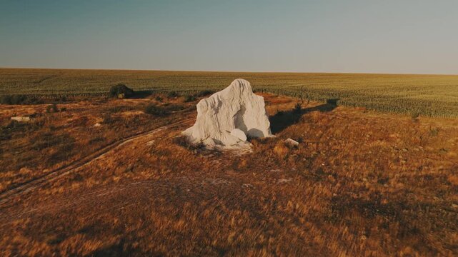 solitary chalk limestone outcrop with rounded boulders at base on dry hill, long shadows toward crop rows.