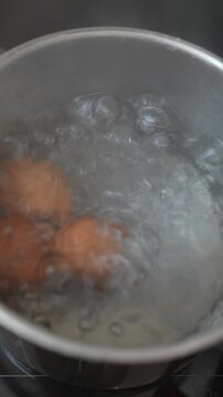 Top-down view of brown eggs boiling in stainless steel pot with vigorous bubbles and rising steam