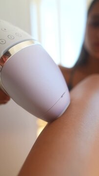 Handheld beauty device applied to bare calf during at-home hair removal treatment with soft window light and shallow depth of field emphasizing product contact care