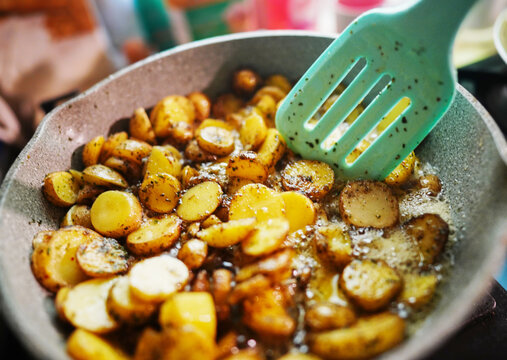Frying sliced ​​potatoes in a pan with added herbs and spices. Appetizing fried potato slices with spices in frying pan. Golden, crispy potatoes being saut&eacute;ed in pan 