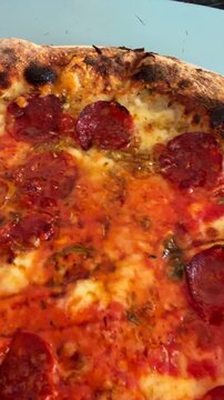 Close-up pepperoni pizza on plate with bubbling melted cheese and pooling tomato sauce, curling pepperoni releasing oil, blistered charred crust with crisp browned edges