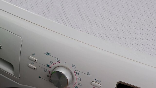 The cleaning process: a person wearing bright gloves wipes the control panel of a household appliance using a rag and a spray bottle, removing dust and dirt from the washing machine.