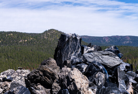 Sharp obsidian rock formations jut out amidst forested hillsides in the Newberry National Volcanic Monument, Oregon.