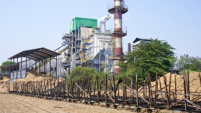 Empty sugarcane transport wagons on rails at Rendeng sugar factory in Kudus, Central Java, Indonesia. Industrial plant with tall chimney and bagasse pile under bright sunny sky in milling season.