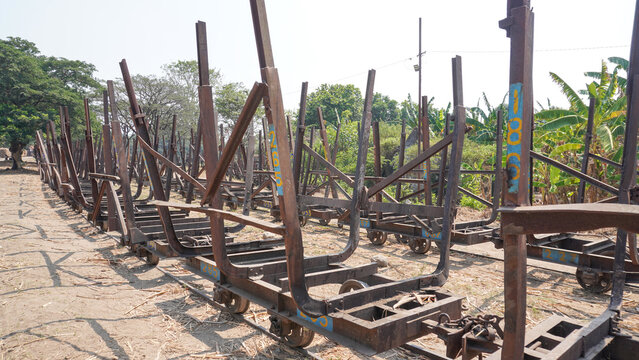 Empty traditional rusty metal sugarcane rail cars parked on narrow tracks at historical Rendeng Sugar Mill in Kudus, Central Java, Indonesia, used for transporting sugar cane during harvest.