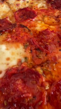 Low angled close up of pepperoni pizza with bubbling melted cheese, glossy oil sheen, and blistered charred crust in wood fired oven setting