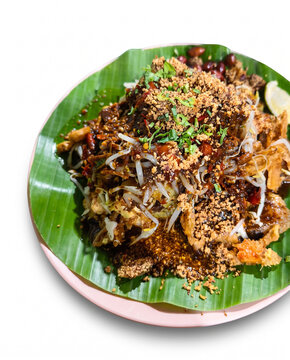Top-down view of Tahu Tek, a traditional East Javanese dish with tofu, bean sprouts, and rich peanut petis sauce, served on a banana leaf over a white background.