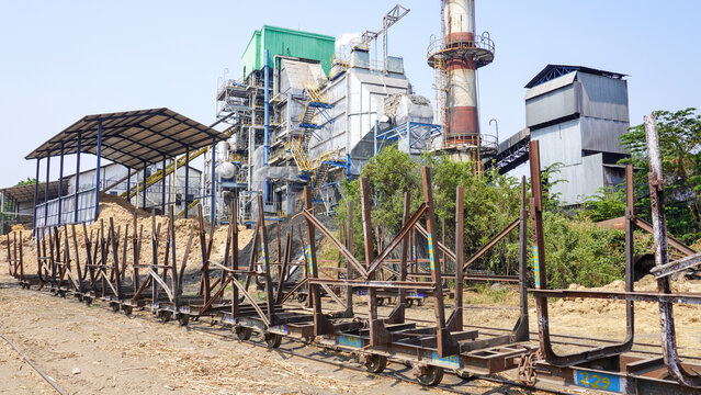 Empty sugarcane transport wagons on rails at Rendeng sugar factory in Kudus, Central Java, Indonesia. Industrial plant with tall chimney and bagasse pile under bright sunny sky in milling season.