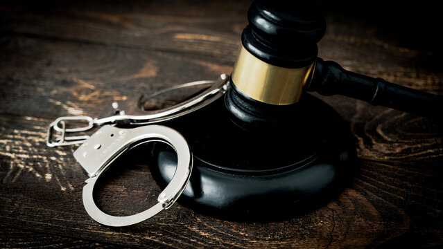 Wooden gavel rests beside silver handcuffs