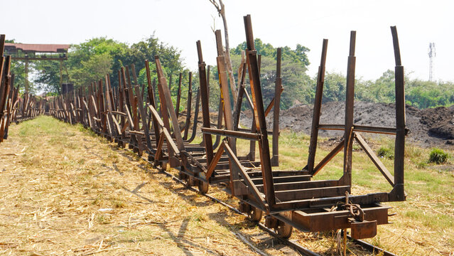 Empty traditional rusty metal sugarcane rail cars parked on narrow tracks at historical Rendeng Sugar Mill in Kudus, Central Java, Indonesia, used for transporting sugar cane during harvest.