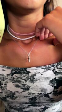Young woman talking on phone while adjusting layered choker and necklace jewelry with cross pendant in warm indoor closeup portrait