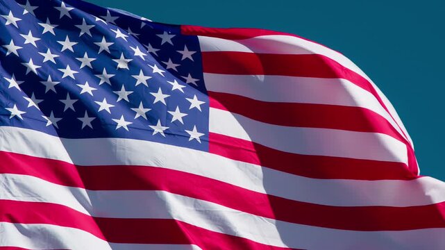 American Flag is Flying in the Wind on a Sunny Day. The Big State Flag is illuminated by the sun and flutters epically in the wind against the blue sky