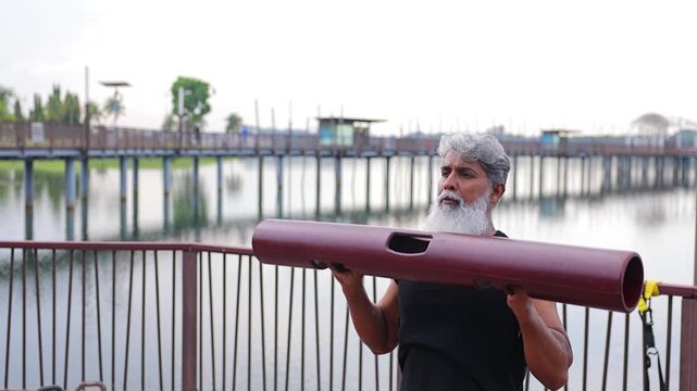 Mature Indian man with a beard exercising in a lakeside park In Singapore.