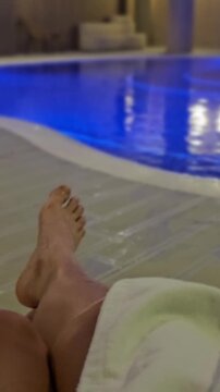 Relaxing by the pool with feet resting on the edge at night with soft lighting and water reflections