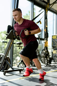 Man Training with Suspension Straps in Modern Gym
